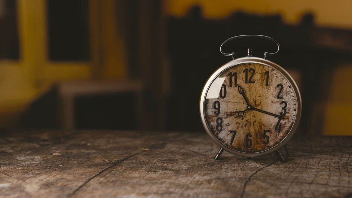 Stary zegar z budzikiem stojący na drewnianym stole